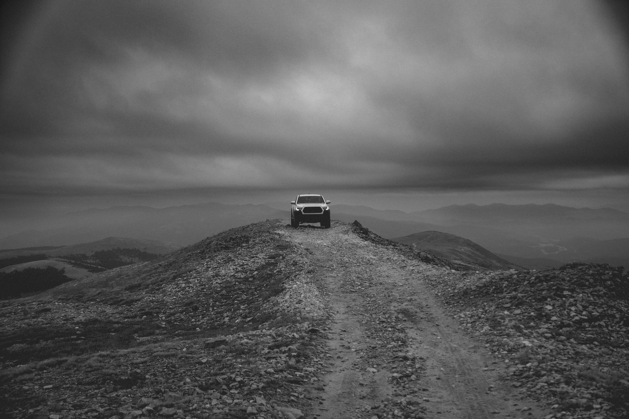 Black and white Toyota Tacoma on mountain ridge summit, vast sky